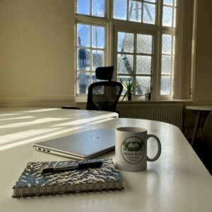 A desk with a notebook, laptop and mug on top