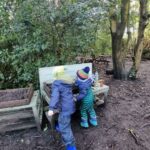 Two children playing at a mud kitchen under trees