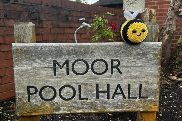 A sign for Moor Pool Hall with a crochet bee on top of it